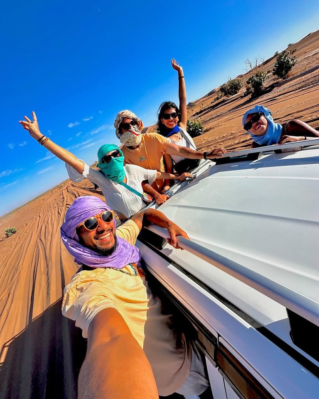 Friends in desert scarves waving from a 4x4 on a Sahara safari with Serenity Sahara