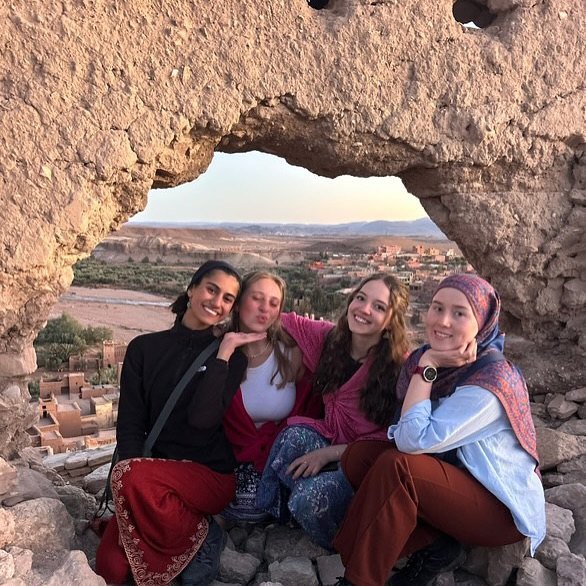 Four Serenity Sahara guests framed by a rock arch above Ait Benhaddou