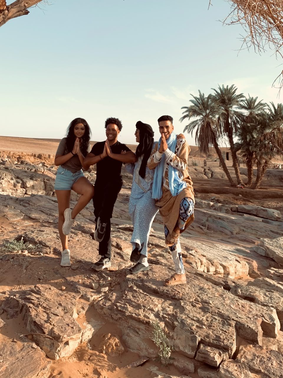 Viajeros y guías de Serenity Sahara haciendo divertidos la postura del árbol junto a un oasis del desierto marroquí