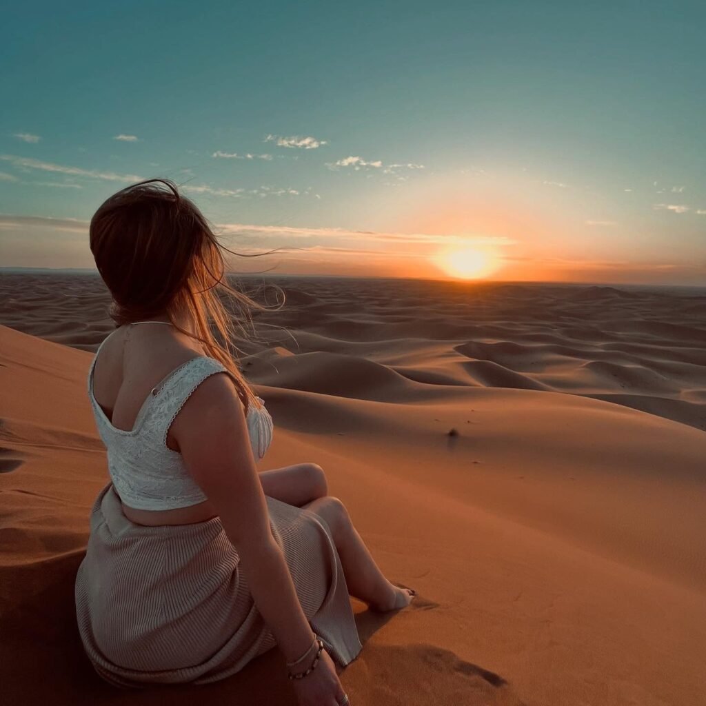 Una viajera sentada en una duna mira la puesta de sol sobre el Sáhara